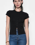 A woman modeling a black short-sleeve knit top with a button-down front and a small front cutout, paired with blue jeans, against a plain light background.