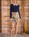 Woman wearing a navy sweater and colorful skirt against a wooden wall.