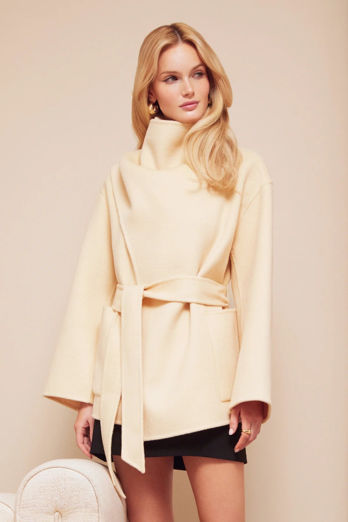 Woman wearing a light yellow coat against a beige background front view