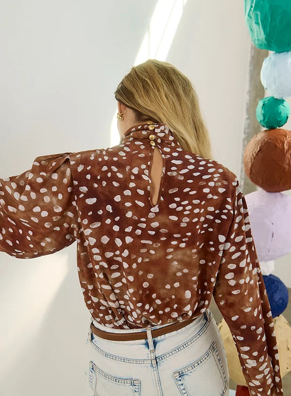 model wearing dapple doe printed top and jeans with art paper mache balls in the background, back view