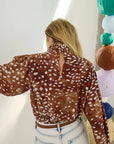 model wearing dapple doe printed top and jeans with art paper mache balls in the background, back view
