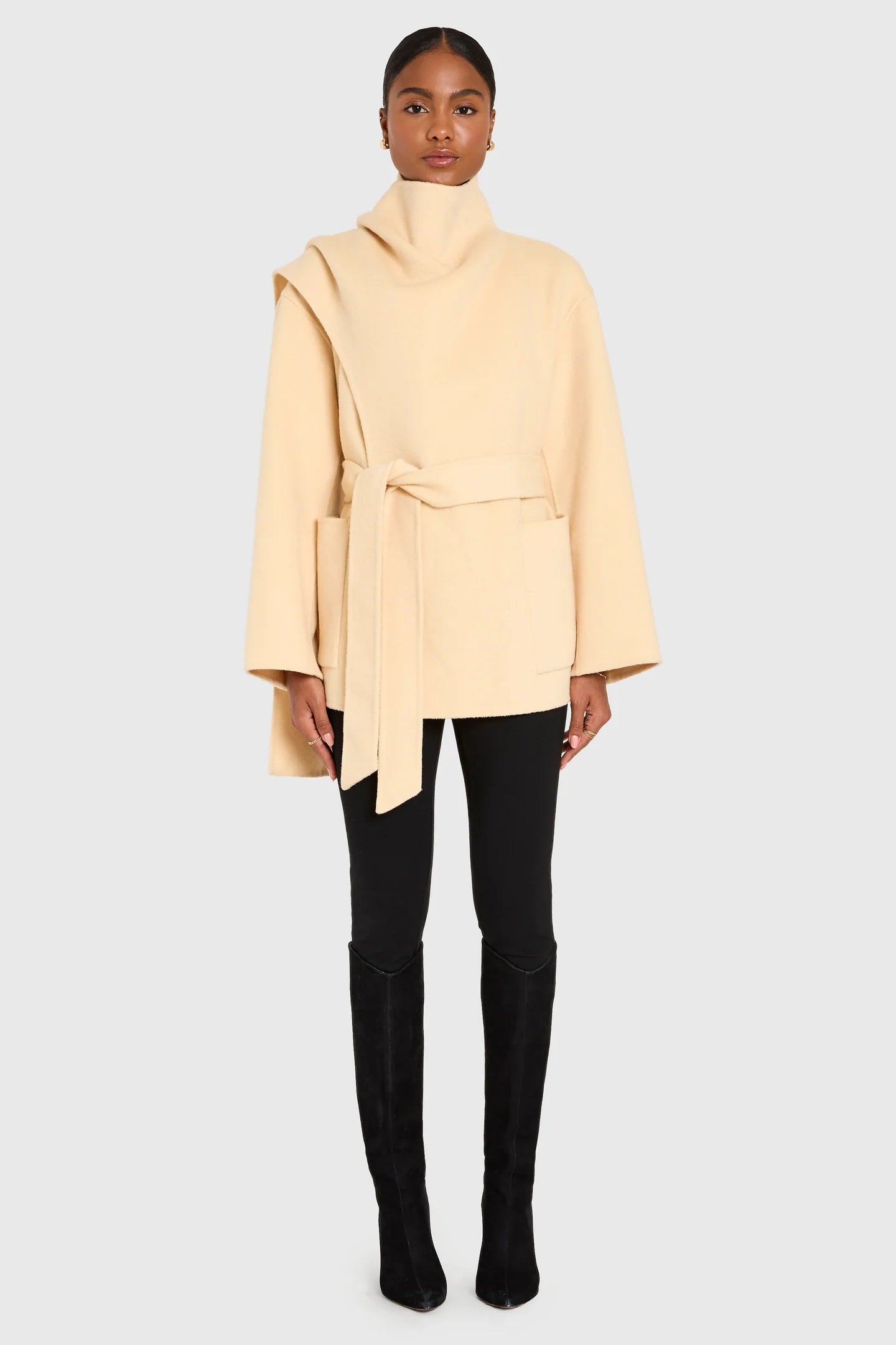 Woman wearing a beige coat, black pants, and black boots on a white background front view