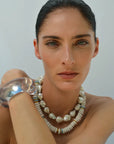 Woman wearing a silver bracelet and pearl necklace against a plain background