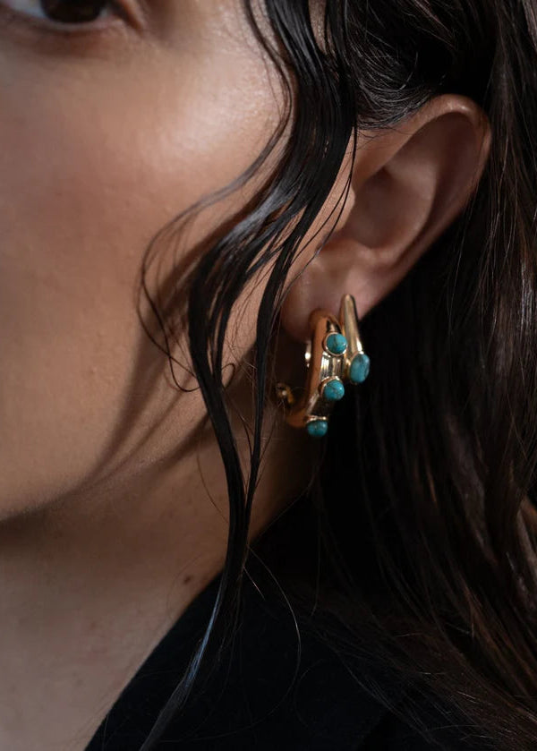 Close-up of a woman wearing gold earrings with turquoise stones.