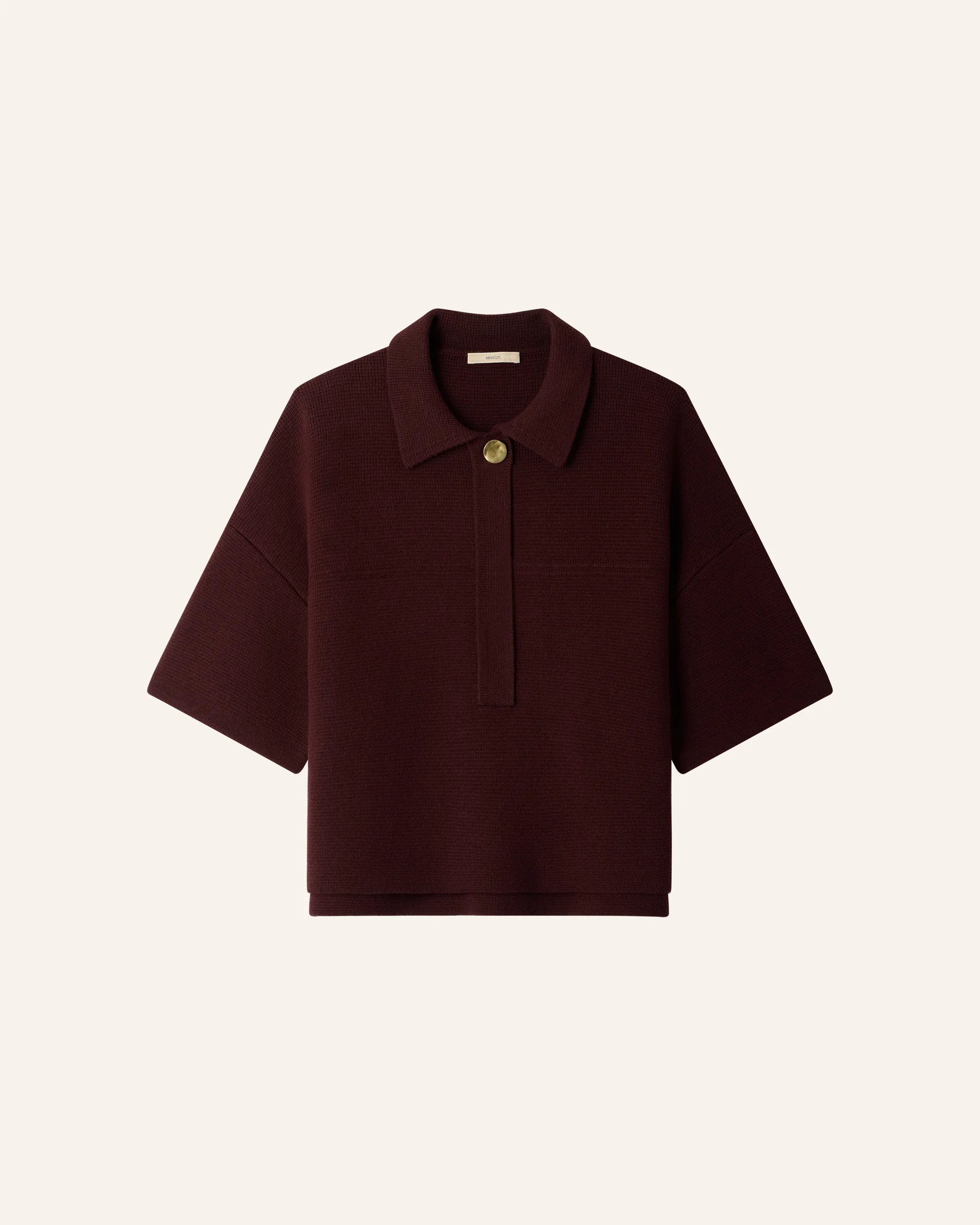 A dark burgundy short-sleeve knit polo shirt with a single gold button, displayed flat against a light cream background.