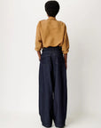 A person shown from the back wearing a mustard yellow vertically striped long-sleeve shirt and dark wide-leg denim jeans against a plain light gray studio background.