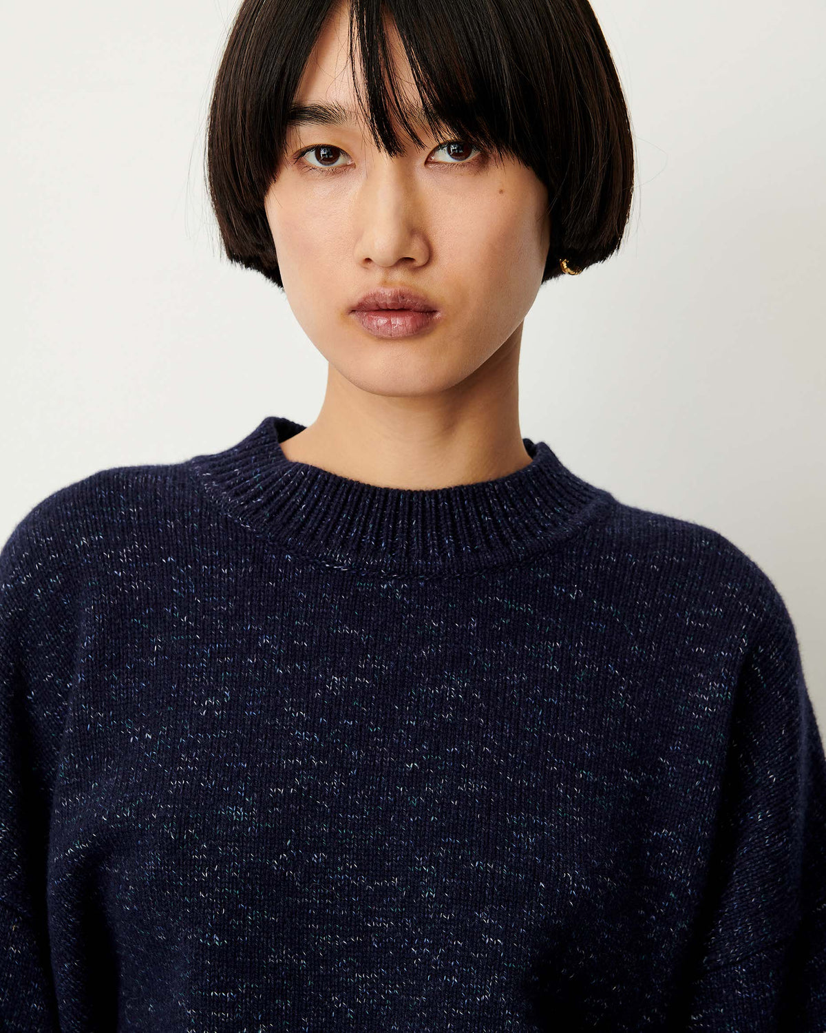 A close-up shot of a model wearing a dark navy blue heathered knit crewneck sweater against a plain light background.