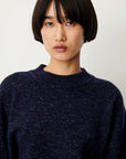 A close-up shot of a model wearing a dark navy blue heathered knit crewneck sweater against a plain light background.