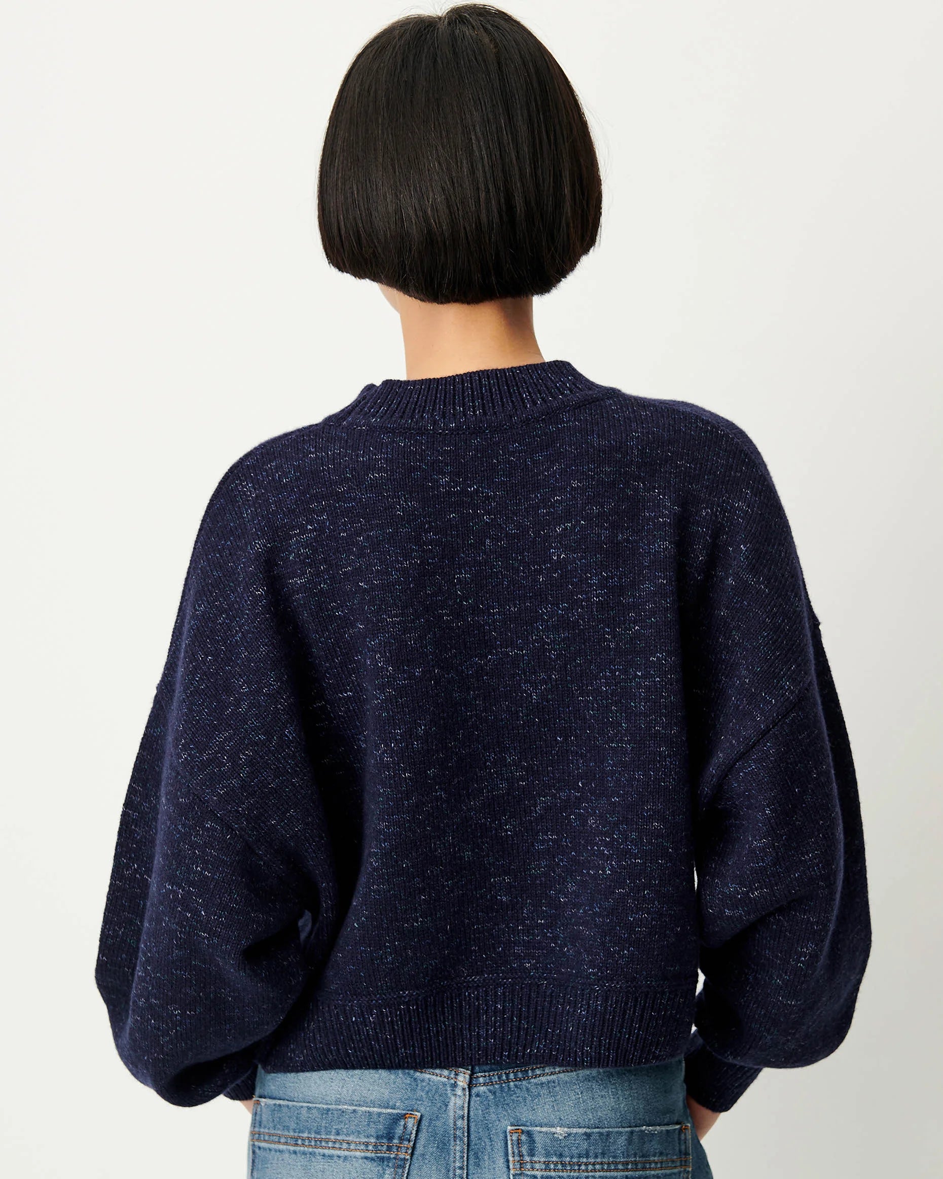 A person shown from the back wearing a dark navy knit sweater with voluminous balloon sleeves and blue jeans, against a plain light background.