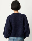 A person shown from the back wearing a dark navy knit sweater with voluminous balloon sleeves and blue jeans, against a plain light background.
