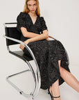 Woman sitting on a modern chair wearing a black patterned dress against a white background