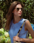 Woman wearing sunglasses and a blue sleeveless top, standing among watermelons.