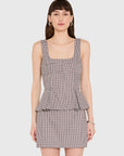 A woman modeling a sleeveless mini set with a square neckline and a peplum waist, featuring a fine brown, beige, and white gingham pattern, set against a solid light gray background.