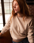 Model wearing Ziggy Sweatshirt Sugar sitting in front of windows and brick wall