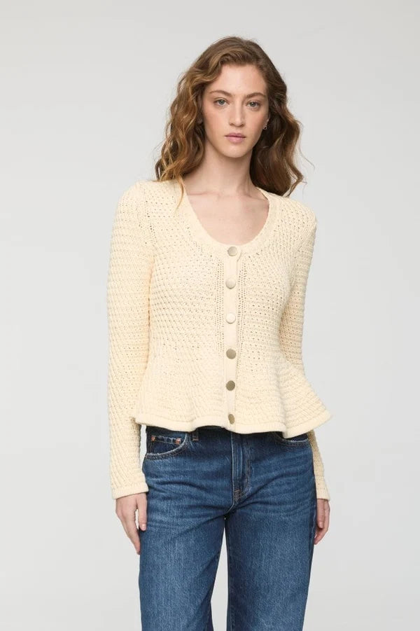 A woman modeling a cream-colored, textured knit cardigan sweater with button-front closure, paired with blue jeans, against a plain light gray studio background.