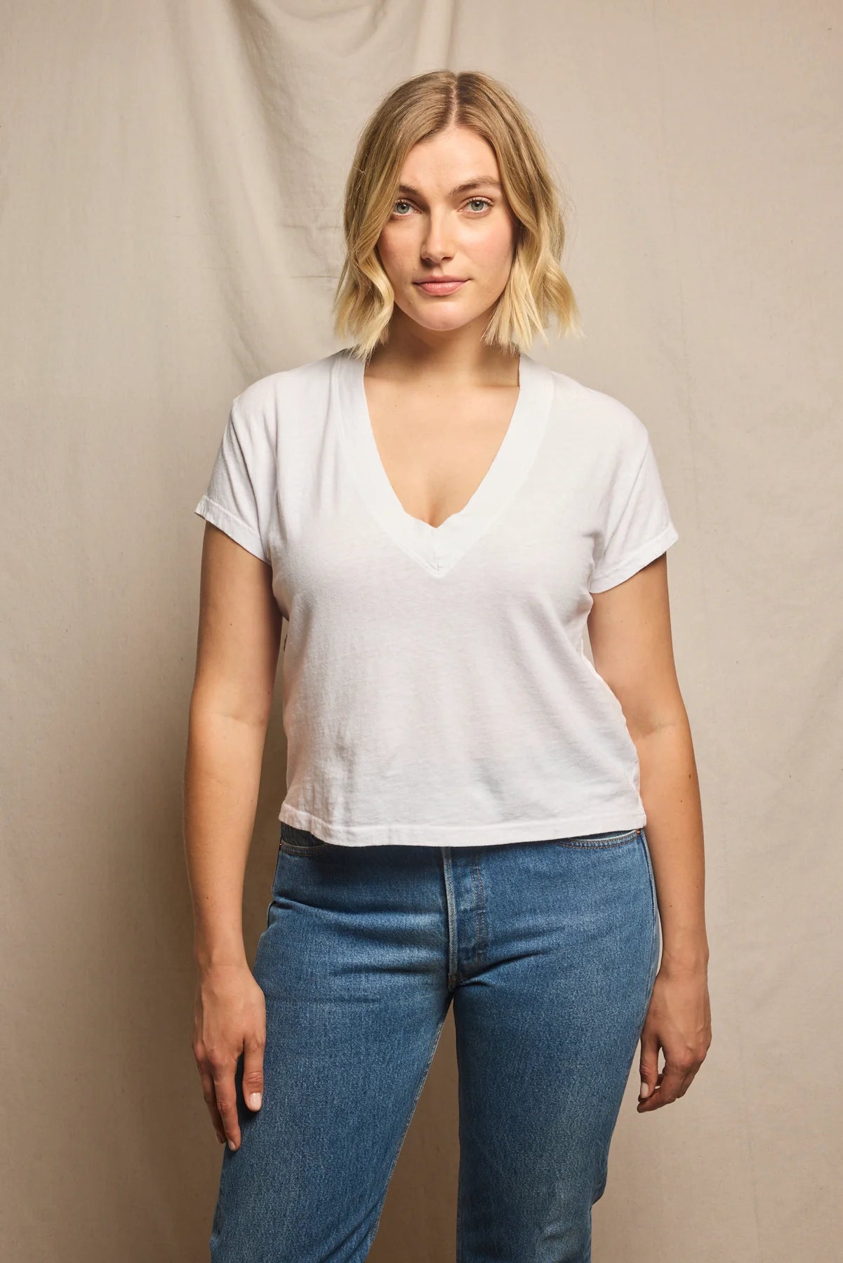 Woman wearing a white t-shirt and blue jeans against a beige background, size L
