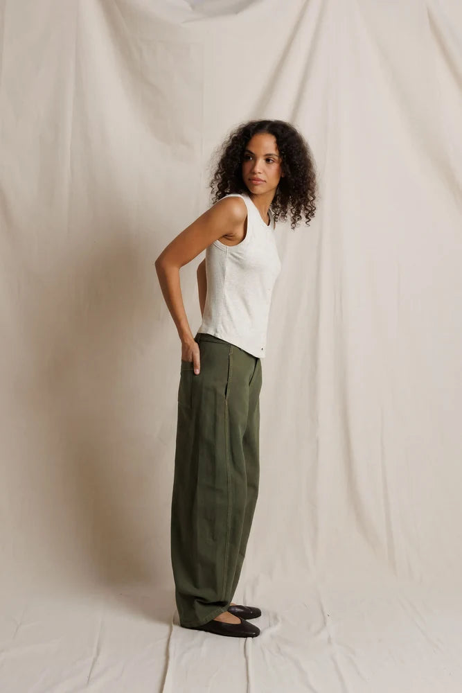 Woman wearing a white sleeveless top and green pants against a plain background