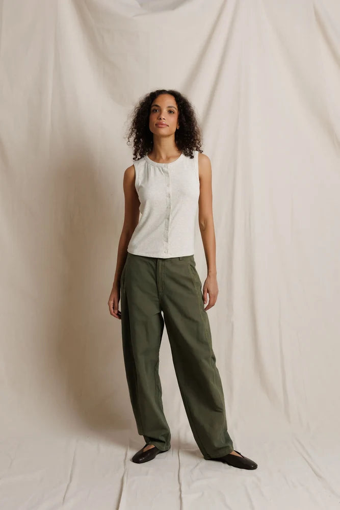 Woman wearing a white blouse and green pants against a plain background