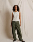 Woman wearing a white blouse and green pants against a plain background