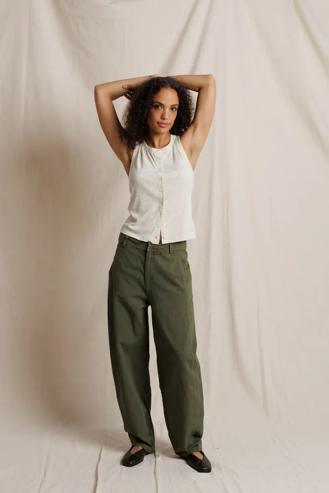 Woman wearing a white sleeveless top and green pants against a plain background