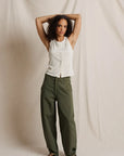 Woman wearing a white sleeveless top and green pants against a plain background