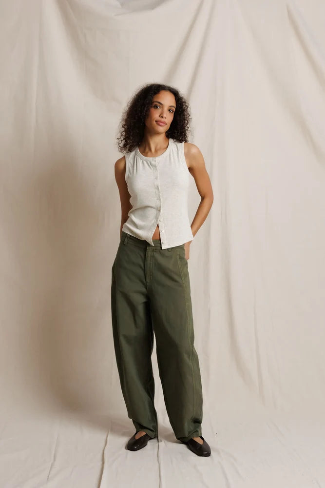 Woman wearing a white sleeveless top and green pants against a plain background