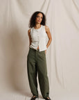 Woman wearing a white sleeveless top and green pants against a plain background