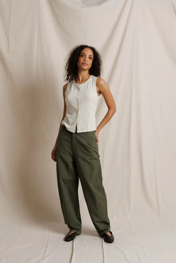 Woman wearing a white sleeveless top and green pants against a plain background