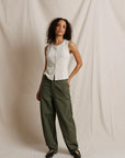 Woman wearing a white sleeveless top and green pants against a plain background