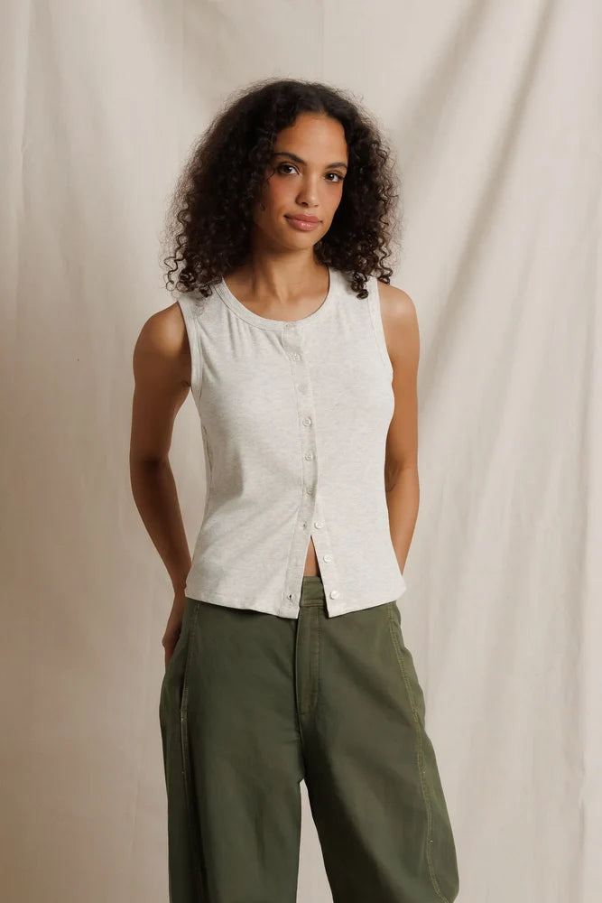 Woman wearing a white sleeveless shirt and green pants against a beige background