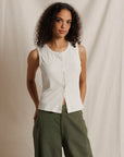 Woman wearing a white sleeveless shirt and green pants against a beige background
