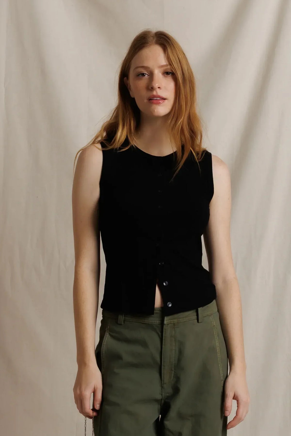 model wearing a sleeveless button down black top with green pants on a cream background