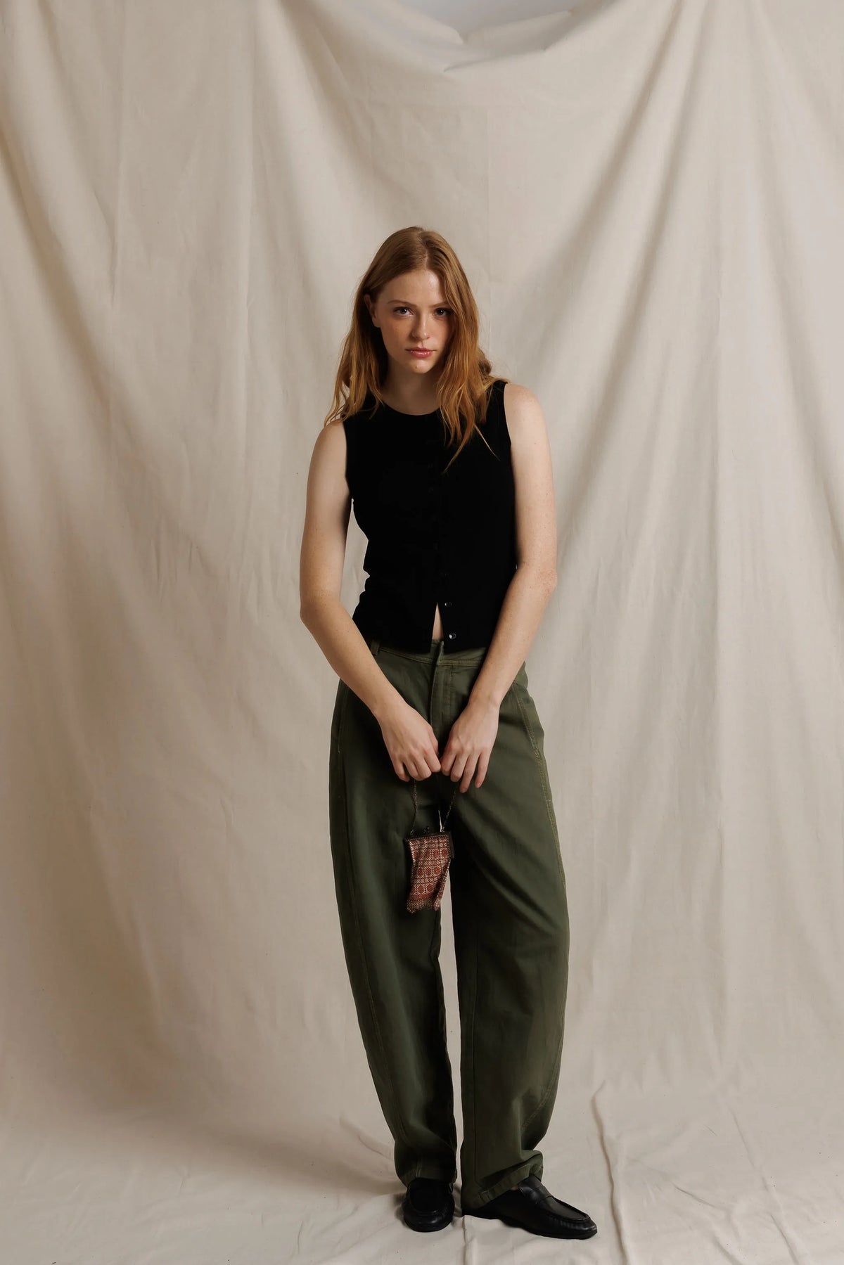 model wearing a sleeveless button down black top with green pants on a cream background