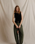 model wearing a sleeveless button down black top with green pants on a cream background