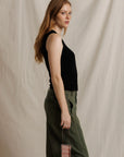 model wearing a sleeveless button down black top with green pants on a cream background, side view