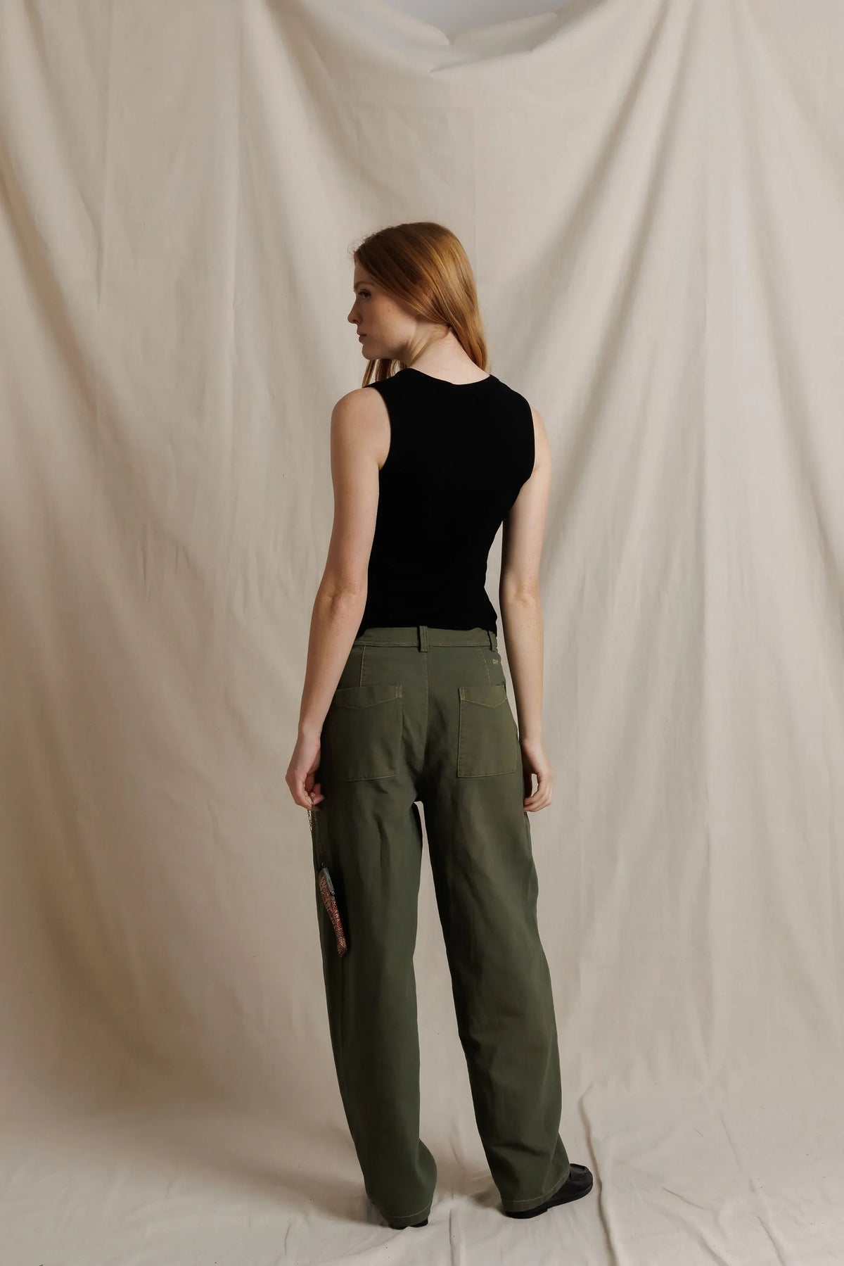model wearing a sleeveless button down black top with green pants on a cream background, back view