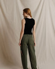 model wearing a sleeveless button down black top with green pants on a cream background, back view