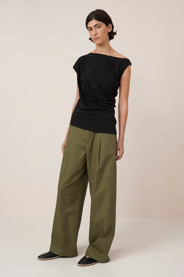 asymmetric top in black on a model with green pants on a cream background