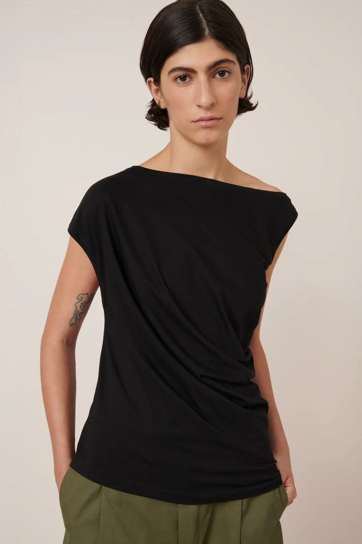 asymmetric top in black on a model with green pants on a cream background