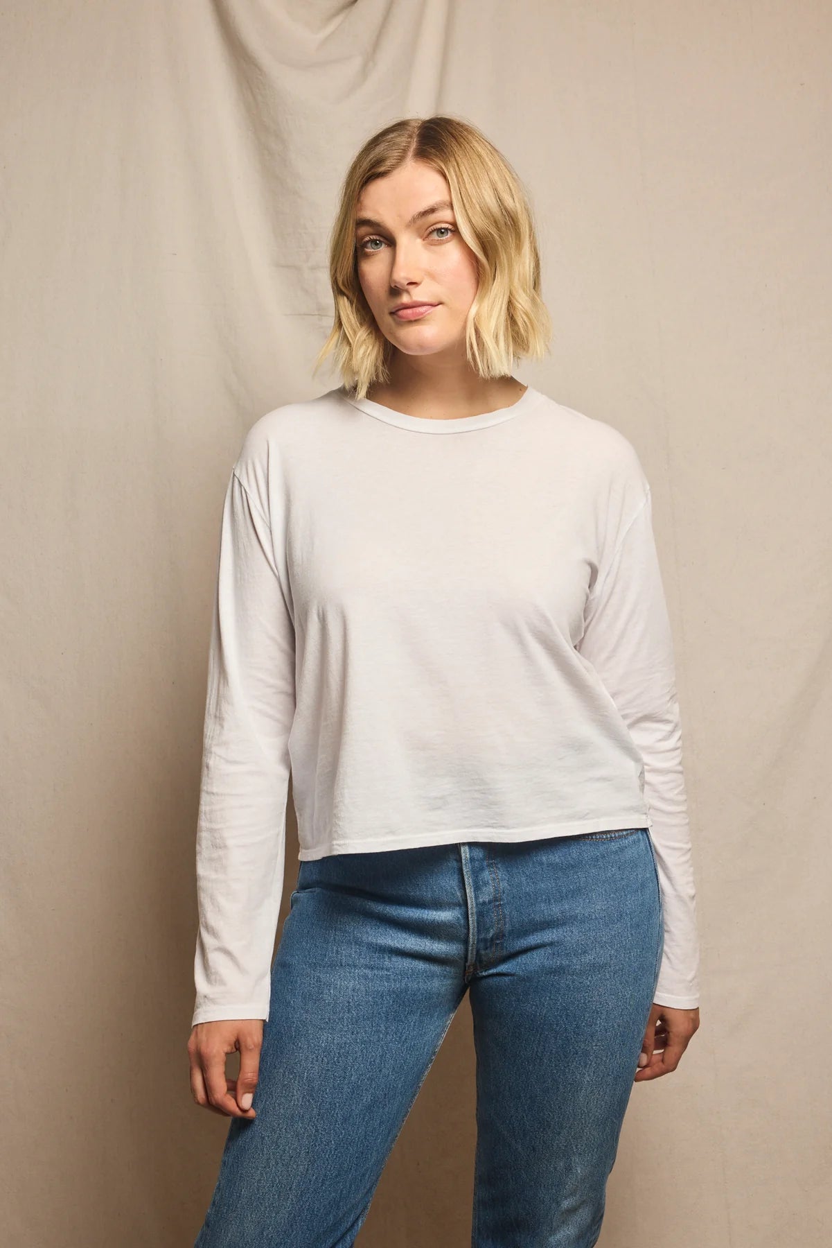 Woman wearing a white long-sleeve shirt and blue jeans against a beige background, size L