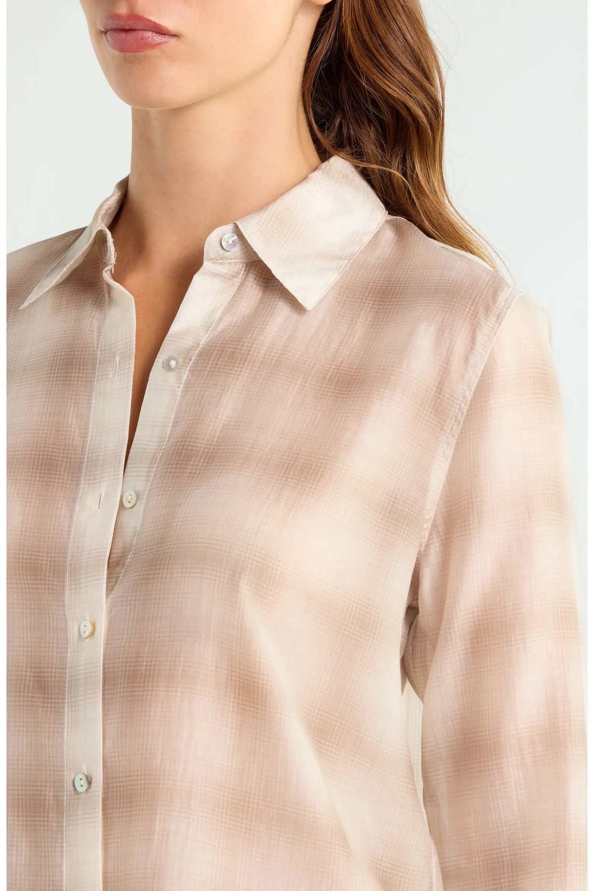 A close-up of a woman wearing a light beige button-up shirt with a subtle textured pattern, showing the collar, buttons, and upper chest area against a plain light background.