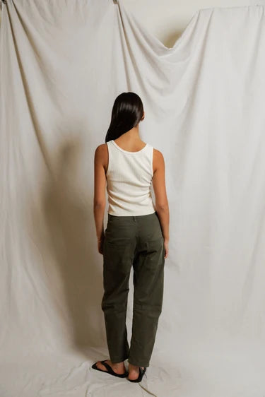 Person wearing a white tank top and green pants standing against a plain white background