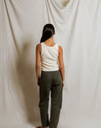 Person wearing a white tank top and green pants standing against a plain white background