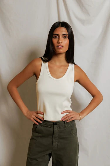 Woman wearing a white tank top and green pants against a plain background