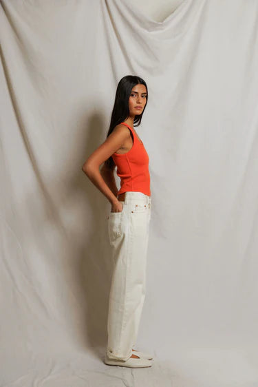 Woman wearing an orange top and white pants against a plain background