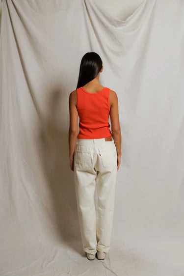 Person wearing a red top and white pants standing against a plain background