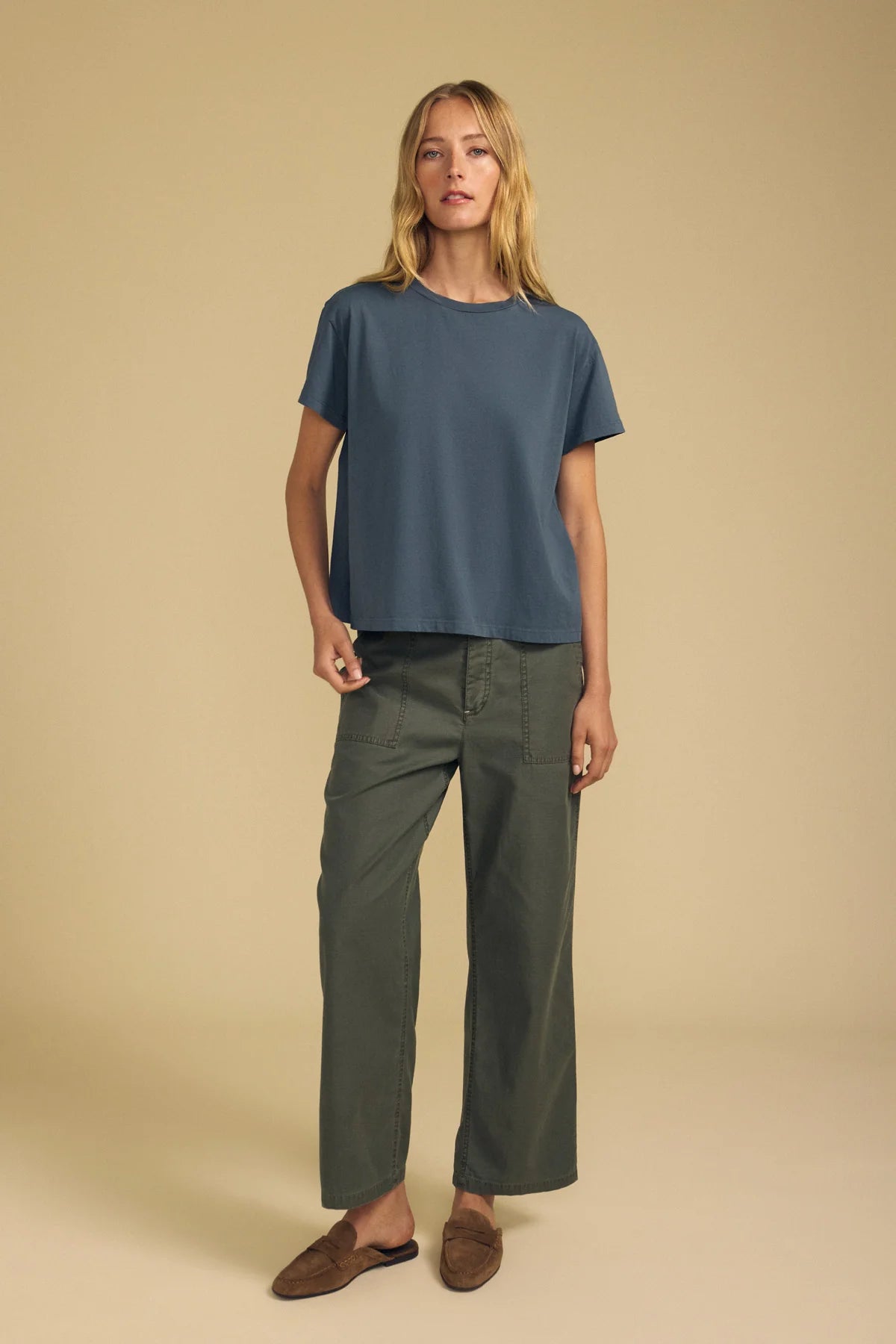 A woman modeling a slate blue short-sleeve crop top and olive green wide-leg pants against a solid beige studio background.