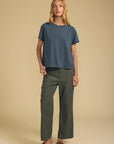 A woman modeling a slate blue short-sleeve crop top and olive green wide-leg pants against a solid beige studio background.