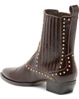 A dark brown leather ankle boot with a pointed toe, stacked block heel, and decorative gold-tone studs along the shaft and around the ankle opening, shown from a side-rear angle on a white background.