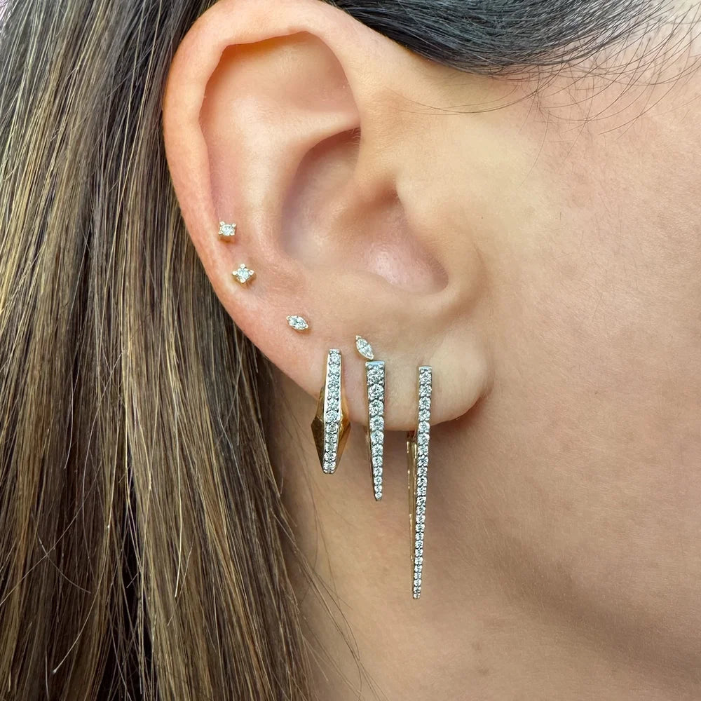 A close-up of a person's ear wearing a pair of long, dangling diamond earrings with multiple thin vertical strands.